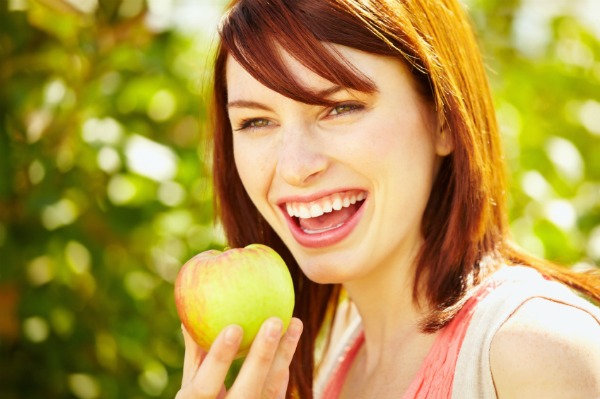 Closeup portrait of beautiful young woman eating apple in park