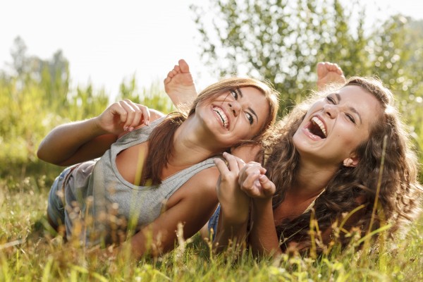 two girlfriends in T-shirts lying down on grass laughing having good time